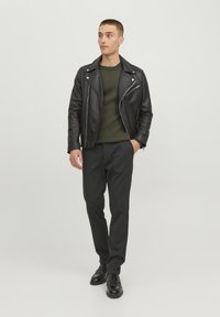 Veste de motard en cuir noir, pull en tricot vert, pantalons gris à motifs et chaussures noires. Design simple avec une texture lisse et une coupe ajustée.