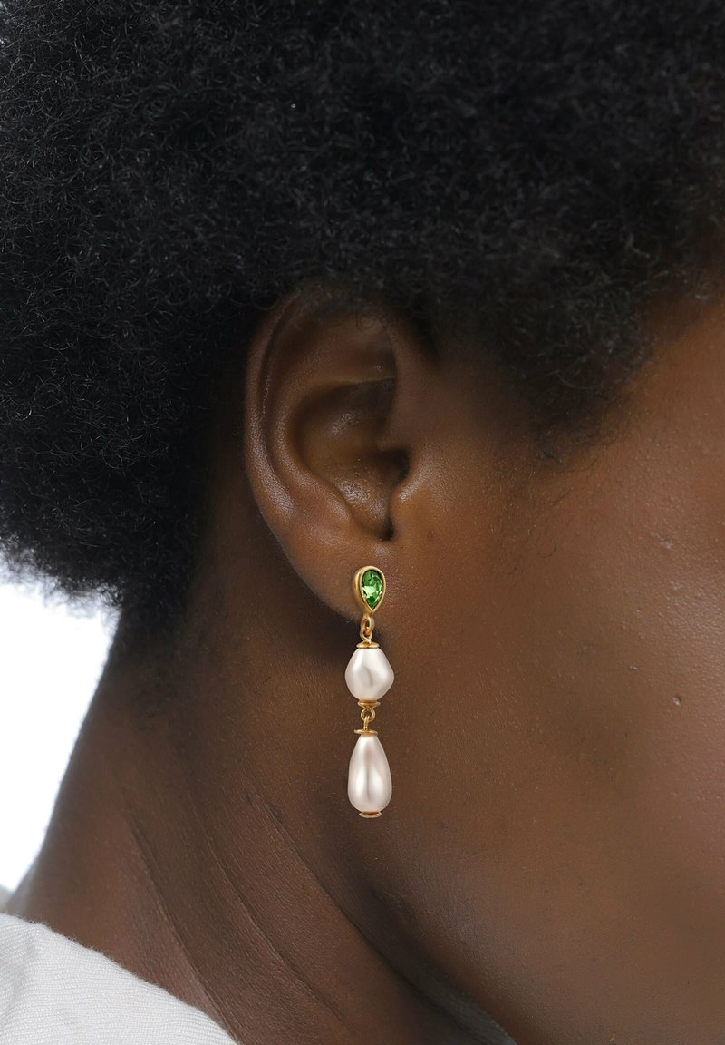 Ohrringe in goldfarbener Ausführung mit einem grünen Edelstein oben, an dem zwei längliche, glänzende weiße Perlen darunter hängen. Glatte, polierte Oberfläche.