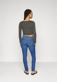 Sötét szürke bordázott, hosszú ujjú cropped felső, kék skinny farmernadrág vissza zsebekkel párosítva. A modellen lapos szandál van.
