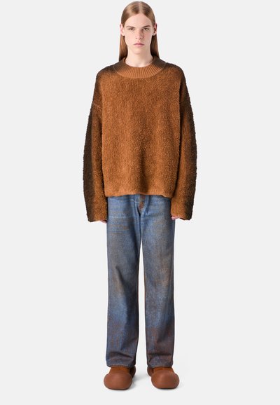 Pullover marrone con texture e taglio morbido, abbinato a jeans blu sbiaditi e scarpe slip-on marroni. Semplice scollo rotondo, senza motivi visibili.