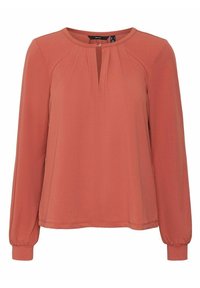 Blouse à manches longues ample en orange rouille. Elle présente un col rond, une petite ouverture en forme de clés et des manches froncées pour plus de texture.