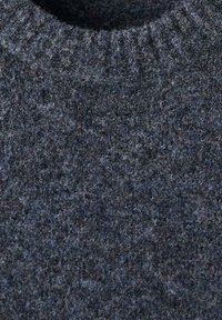 Dettaglio ravvicinato di un maglione in lana grigio scuro con un colletto a girocollo a coste e tessuto a maglia testurizzato.