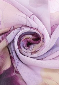 Tessuto di seta in tonalità di rosa e viola, con motivi floreali e una texture liscia, artisticamente arrotolato in una spirale.