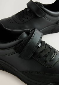 Sorte sneakers lavet af læder og mesh, med snørebånd og en velcro-rem, der har en struktureret sål og perforeringer nær tåen.