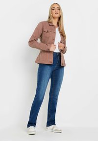 Veste en denim rose clair avec un col, des poches avant et des boutons. Associée à un jean bleu foncé et des baskets blanches.