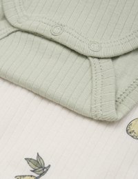 Jasnozielony prążkowany body dla niemowląt z zapięciem na napy, założony na kremową tkaninę z wzorem cytryny i liści.