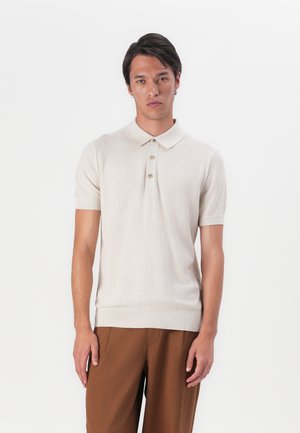 Beige knitted polo shirt with short sleeves, three button placket, ribbed collar and hem. Paired with brown trousers.