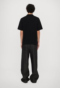 Cămașă polo neagră cu o croială lejeră, mâneci scurte și guler, asociată cu o pereche de pantaloni largi de culoare gri închis. Design simplu, fără modele.