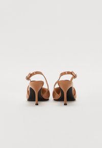 Sandales à talons hauts beiges avec un dessus en cuir verni, une bride de cheville et un talon aiguille noir élancé, présentant une texture lisse et un design minimaliste.