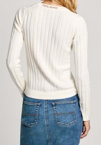 Maglione a coste di colore crema con un design aderente, caratterizzato da un collo rotondo e un logo Pepe Jeans sulla parte posteriore, abbinato a una gonna di jeans.