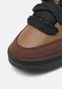 Baskets en cuir marron avec une tige en daim et des lacets noirs texturés, dotées d'une semelle épaisse en caoutchouc noir et d'éléments de design ventilés.