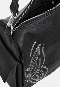 Sac à main en cuir noir avec fermeture éclair argentée, design brodé et clous métalliques. Forme compacte avec surface texturée et bandoulière réglable.