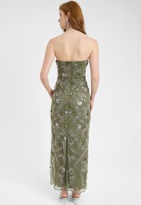 Abito senza spalline verde oliva con ricca ricamo floreale, paillettes e una silhouette aderente con una leggera strascico. Sandali con tacco trasparente.