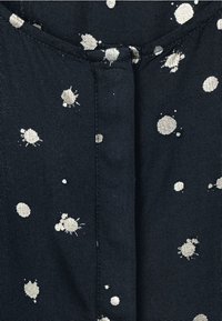 Mörk tyg med utspridda metalliska silverfärgsplatter och sömdetaljering längs halsringningen och mittsömmen.