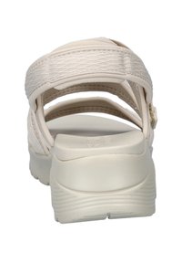 Sandalia beige con correas de tela texturizada y suela blanca gruesa. La plantilla contorneada ofrece soporte. Diseño minimalista con cierre ajustable.