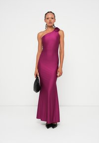 Fuchsia one-shoulder dress made of smooth, stretchy fabric, featuring a floral accent on the shoulder and a fitted silhouette down to the hem.