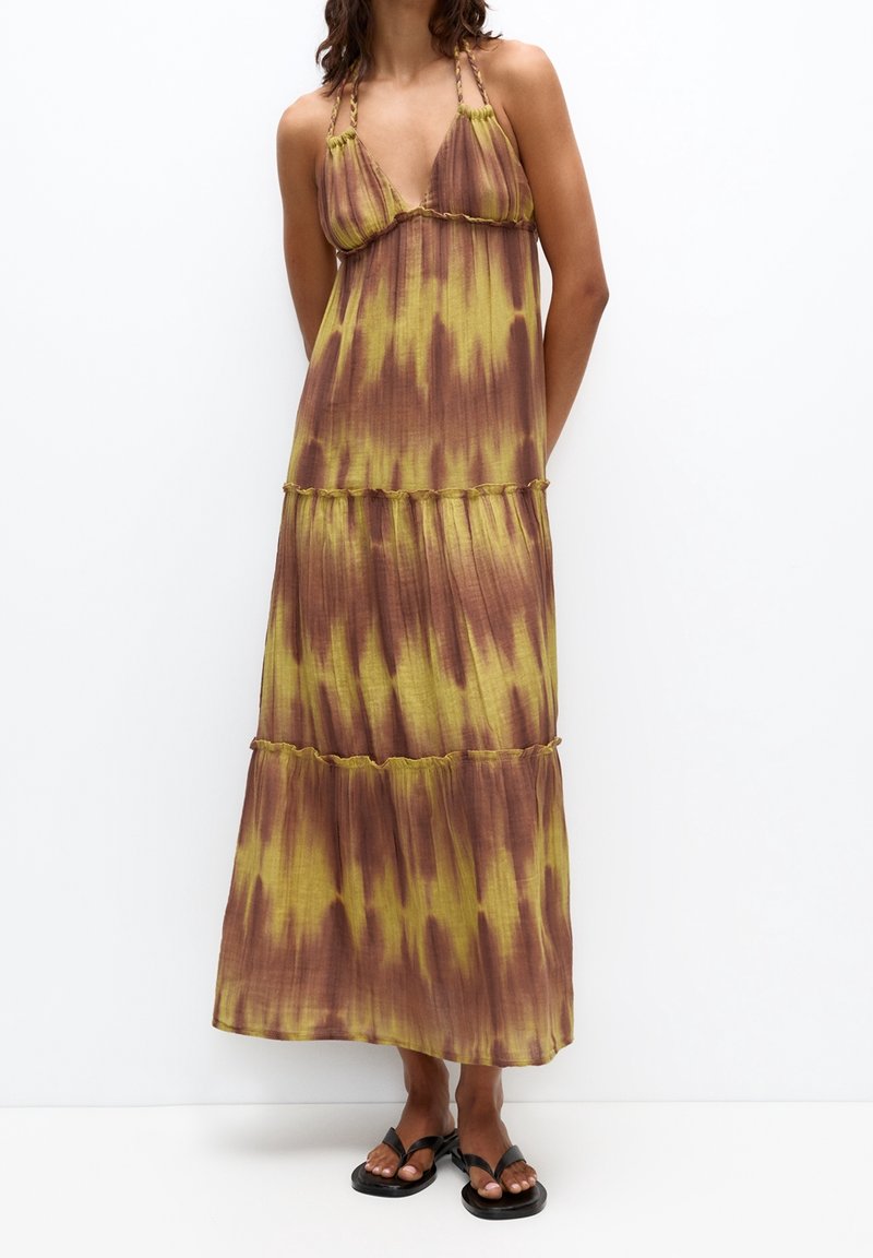 Robe longue avec un décolleté en V profond, bretelles nouées et design à étages. Présente un motif tie-dye aux nuances vertes et brunes, fabriquée en tissu léger.