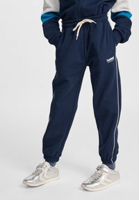 Navyblå sweatpants med elastisk midja och dragband. Har vita sidestreck och "hummel"-logotyp. Tillverkad av mjukt material.