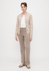 Bežs adīts kardigāns ar apaļu kakla izgriezumu un pogām, uzvilkts virs baltas blūzes, kombinēts ar bežām sporta biksēm un kedām. Neitrāla krāsu palete.