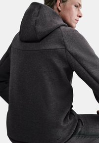 Felpa con cappuccio grigio scuro con texture liscia e design minimalista, caratterizzata da un dettaglio ricamato sul giogo e un logo Nike discreto.