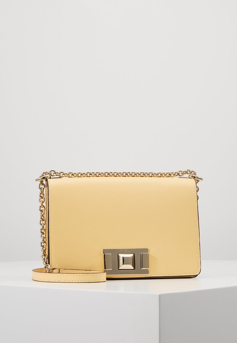 Yellow leather handbag with gold chain strap and square gold clasp, displayed on a white pedestal against a plain background.