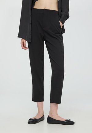 Pantaloni neri su misura con vita alta, caratterizzati da pieghe e tasche laterali, abbinati a ballerine nere piatte. Tessuto liscio.