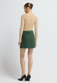 Beige geribbelde lange mouwen top, groene rok met een aansluitende tailleband, en zwarte hoge hakken met een gestructureerde afwerking.
