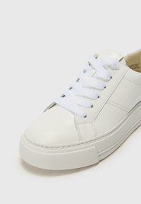 Hvite sneakers laget av glatt skinn med flate hvite snørebånd, gummisåle og subtile sømdetaljer. Har et minimalistisk design.