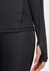 Svart långärmad träningsöverdel gjord av mjukt, sträckbart tyg. Har en texturerad panel på ärmen och en åtsittande passform vid midjan.