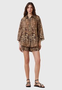 Set di camicia e pantaloni corti con stampa leopardata in tessuto leggero. Presenta un colletto, chiusura a bottoni e una vestibilità rilassata. Sandali neri completano l'outfit.