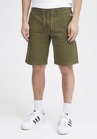 Olivgröna shorts med elastisk midja och dragsko, med rak skärning och sidfickor. Matcher med vita sneakers.