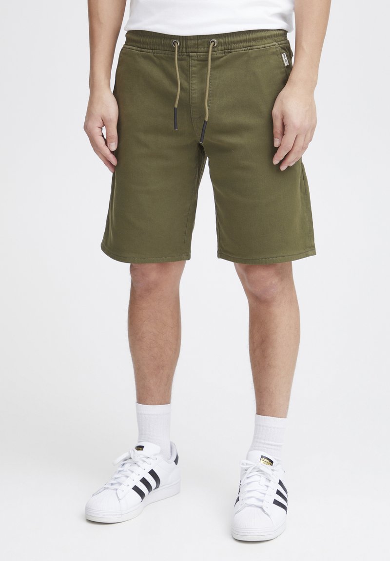 Olivgröna shorts med elastisk midja och dragsko, med rak skärning och sidfickor. Matcher med vita sneakers.