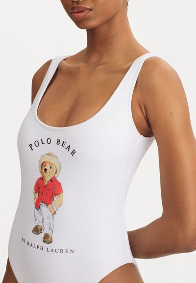 Costum de baie alb, dintr-o singură piesă, cu un urs de desene colorat purtând o cămașă roșie, având textul "POLO BEAR" deasupra și "by Ralph Lauren" dedesubt.