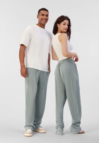T-shirt blanc à manches courtes, pantalon rayé vert clair, baskets décontractées. Le pantalon a une taille élastique ; le modèle pose de dos à dos.