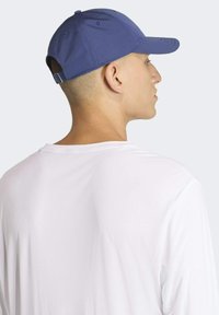 Modrá baseballová čiapka vyrobená z látky s zakriveným štítom, nastaviteľný remienok vzadu, nosená s bielym tričkom.