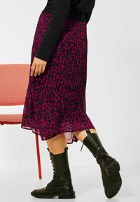 Una gonna plissettata di un blu navy scuro con un vivace motivo animalier rosa, abbinata a stivali in pelle nera con lacci fino al ginocchio.