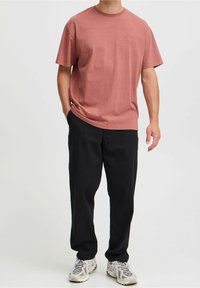 Camiseta de algodón de manga corta color rosa con cuello redondo y logo sutil en el frente, combinada con pantalones negros y zapatillas de color claro.