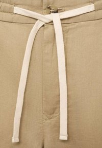 Pantalons en lin beige avec une taille à cordon, dotés d'une fermeture à bouton rond et d'une surface légèrement texturée.