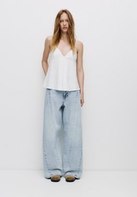 Witte, mouwloze top met een V-hals en een uitlopende ontwerp, gecombineerd met lichtblauwe, wijde denim broeken. Beide kledingstukken hebben een ontspannen pasvorm.