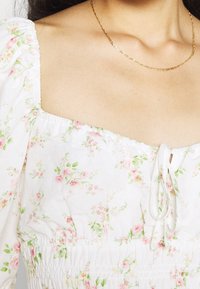 Top de algodón floral con mangas abullonadas, escote cuadrado y cintura fruncida. Decorado con pequeños patrones de flores rosas y verdes.
