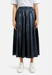 Black, pleated midi skirt made of shiny, textured fabric, featuring an elastic waistband and worn with white sneakers.