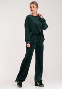 Ciemnozielony dres z weluru, składający się z luźnej bluzy z długim rękawem oraz tapered spodni z elastycznym pasem i sznurkiem. Czarne sneakersy dopełniają cały strój.