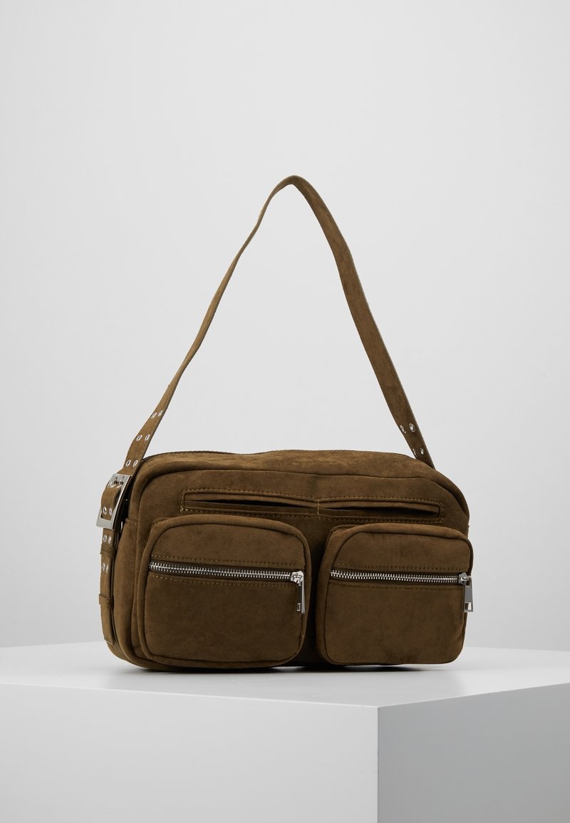 Sac à bandoulière en daim marron avec deux poches avant zippées et une bandoulière ajustable présenté sur un socle blanc.