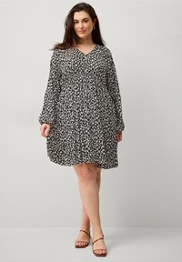 Schwarzes Blumenkleid mit langen Ärmeln, V-Ausschnitt, gerafftem Bund und ausgestelltem Rock; hat kleine weiße Blattmuster im gesamten Kleid.