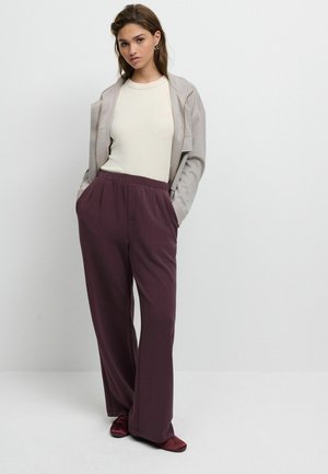 Lichtgrijze zip-up jack over een crèmekleurig top, gecombineerd met loszittende bordeauxrode broek. Zachte stof met een elastische taille en zijzakken.