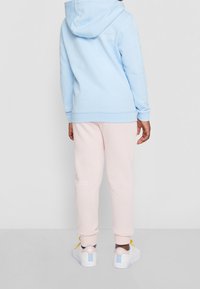 Ljusblå hoodie med dragsko, rosa sweatpants och vita sneakers. Hoodien har ett mönstrat ärmmotiv och en logodetalj på ryggen.