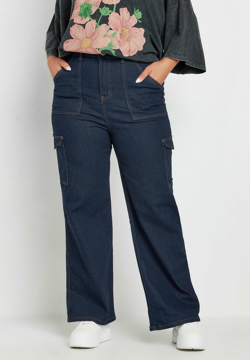 Tummansiniset cargo-housut, joissa on leveät lahkeet, kontrastitikkaus, sivutaskut ja rento istuvuus, yhdistettynä kukkakuosisella t-paidalla ja valkoisilla tennareilla.