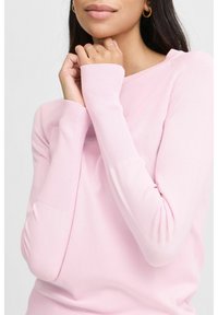 Hellrosa Pullover mit langen Ärmeln, gerippten Bündchen, Rundhalsausschnitt und weicher Textur, entworfen für einen figurbetonten Look. Nahaufnahme der Arme.