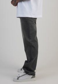 Jeans din denim gri, cu o croială relaxată, asortați cu adidași albi ce au accente gri și detalii texturate.