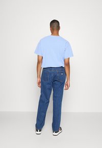 Light blue cotton t-shirt, short sleeves, with loose-fit dark blue denim jeans, featuring back pockets and a small brand patch. White sneakers.